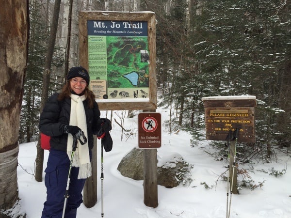 woman in winter coat with trekking poles in front of sign for mt. jo trail