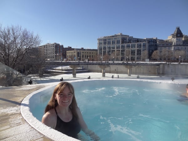 woman in black bathing suit in pool with old montreal limestone buildings in background