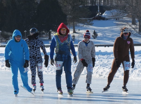 Five people in warm suits skating outdoors on a lake.