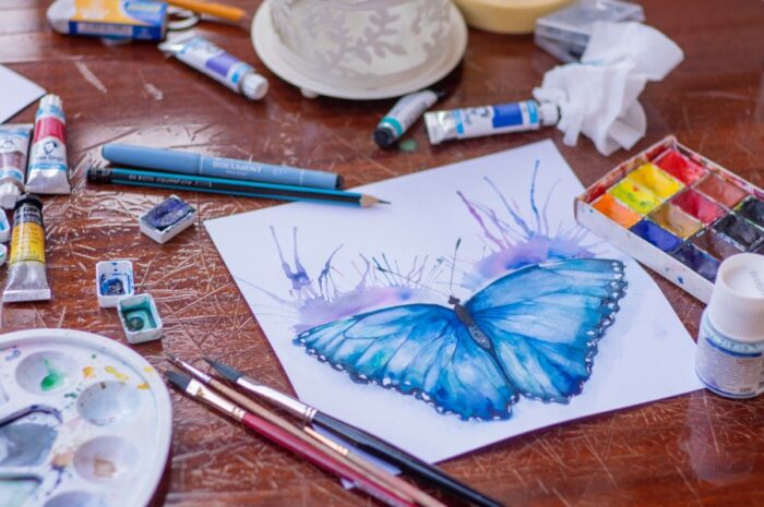 half-finished watercolour painting of a butterfly, surrounded by artists' materials