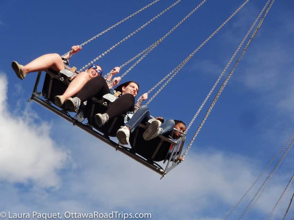 three teenagers on a fair swing high in a blue sky