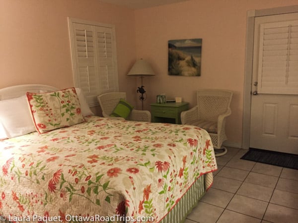 Bed with floral cover and two rattan chairs in English Garden room at Windemere Inn by the Sea in Indialantic, Florida.