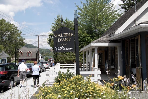 Art gallery sign and people strolling past small shops on rue Principale in Saint Sauveur, Quebec.