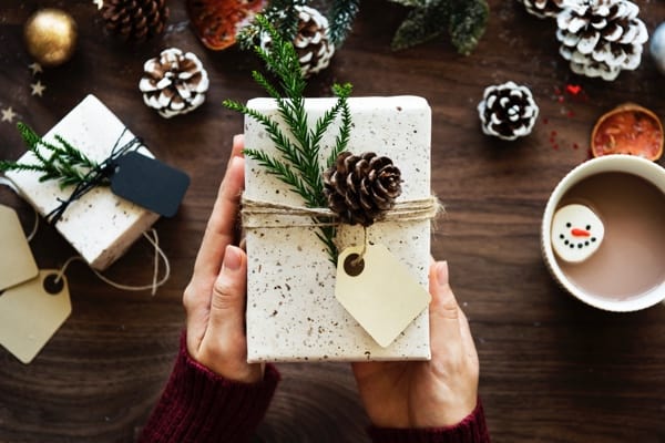 Christmas present wrapped in white paper with pinecone and greenery.