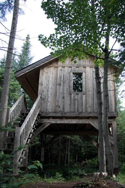 Weathered wooden treehouse at Les Refuges Perchés in Quebec.
