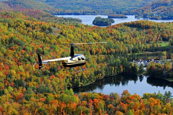 helicopter flying above hills covered in fall foliage, with lakes, in the laurentians area of quebec.