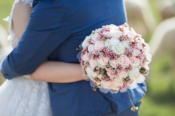 Couple hugging with round wedding bouquet. Photo by Orio Nguyen on Unsplash.