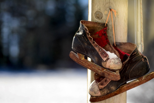 Vintage leather hockey skates hanging on a wooden post.