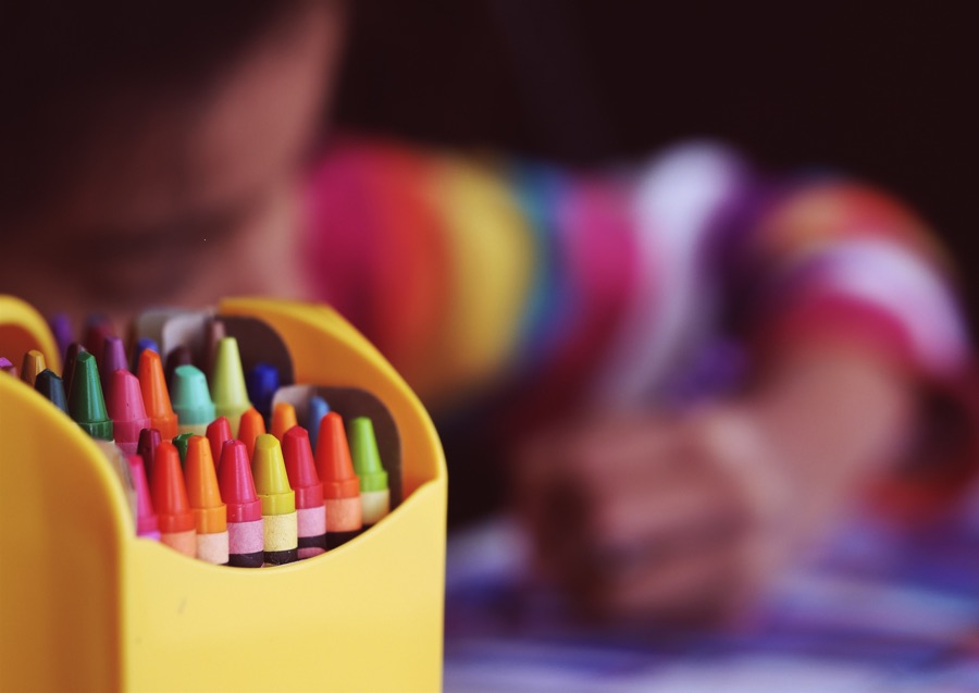 crayons in foreground with child colouring in background