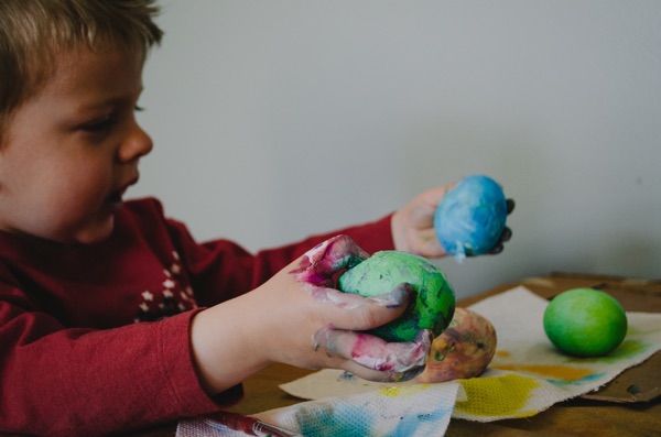 child sitting at a table with painted eggs in his hands. photo by kelly sikkema on unsplash.