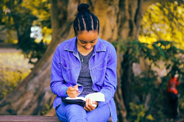 Woman sitting outside under a tree reading a book.