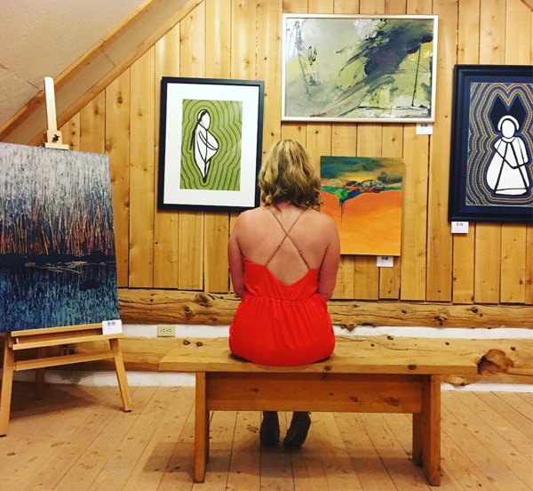 Woman in red dress looking at wall of artworks.