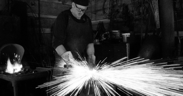 Blacksmith at a forge making a piece showing an osprey catching a trout.