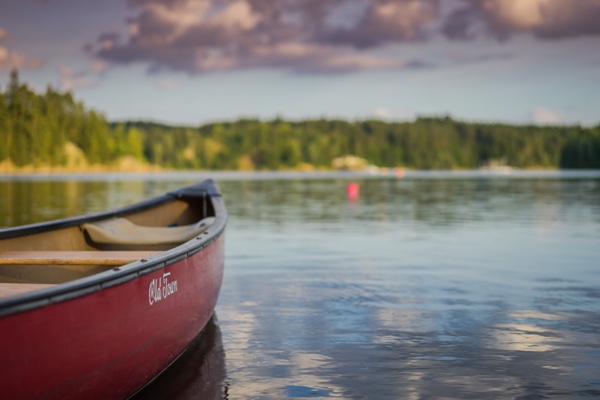 Tip of the bow of a red canoe on a wood-fringed lake.