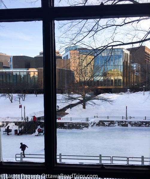 a huge window outside the senate chamber offers a great view of the national arts centre and a skater on the rideau canal in ottawa.