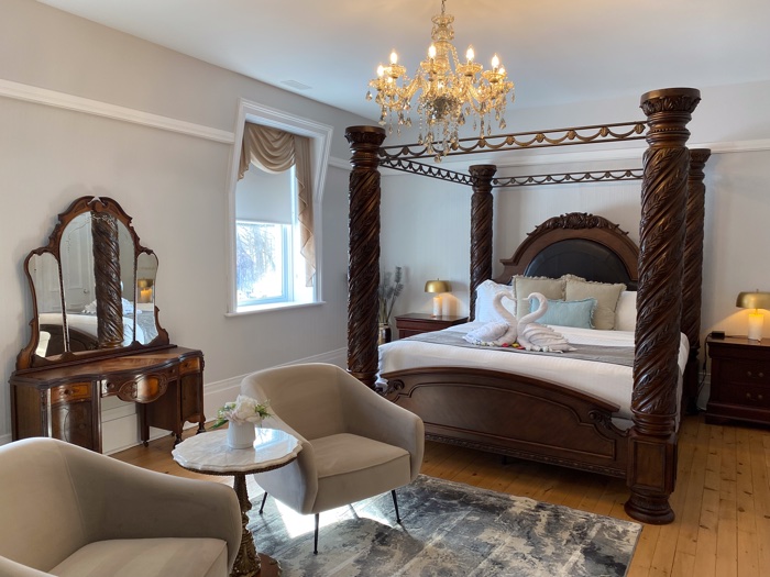 hotel room with chandelier, four-poster bed, antique dressing table and beige chairs