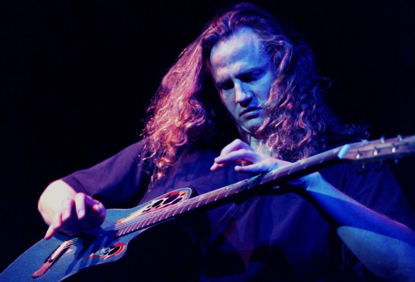 Photo of Preston Reed playing guitar under a blue stage light.