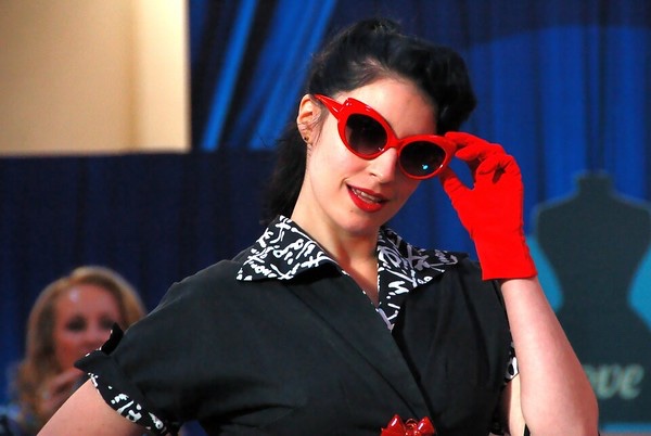 Model in black-and-white 1950s dress with red sunglasses and red gloves.