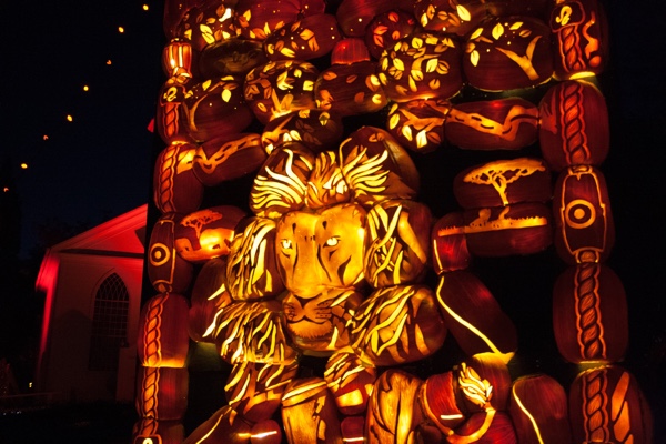 illuminated lion made of artificial orange pumpkins, with an old white church illuminated with red light in the background.