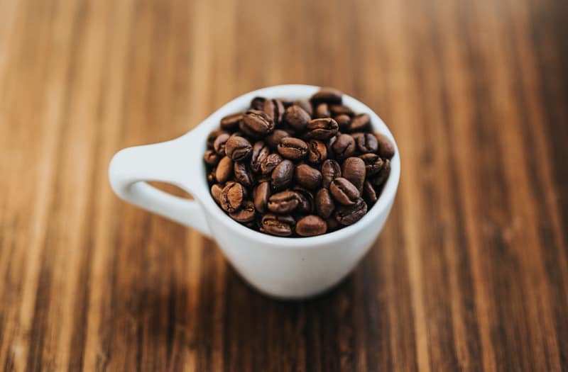 coffee beans in a white mug on a wooden tabletop