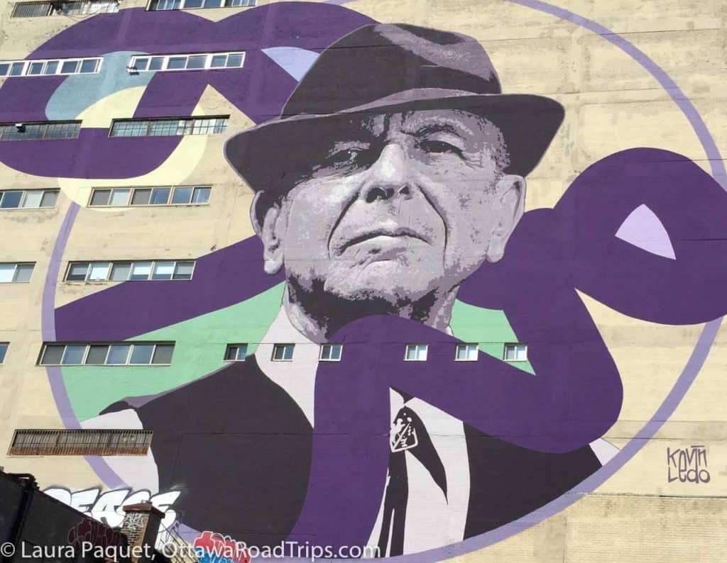 mural on a beige building of leonard cohen wearing fedora and suit.