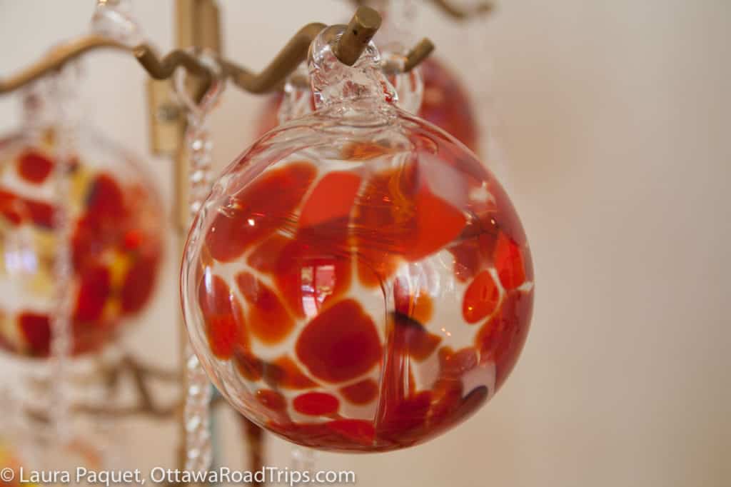round clear glass christmas ornament with red pattern hanging on a brass stand, at gray art glass in merrickville, ontario.