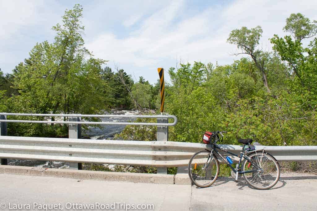blue bike resting against a metal bridge over a river near almonte, ontario.