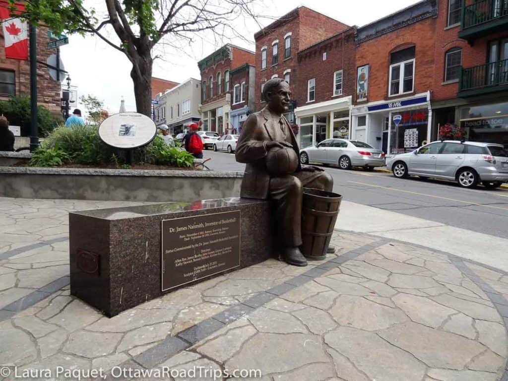 sculpture of james naismith with small shops in background in downtown almonte, ontario