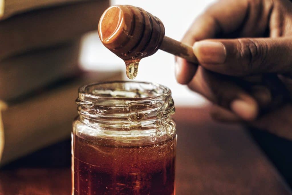 hand holding a honey dipper above a full jar of honey
