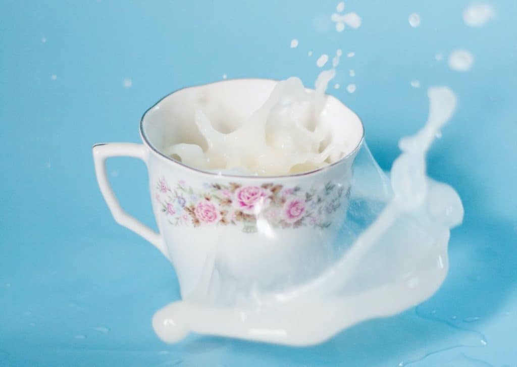 pink-flowered china teacup with milk splashing out of it, against a blue background.