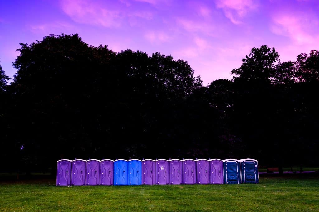 Blue and purple portapotties in a field at sunset.