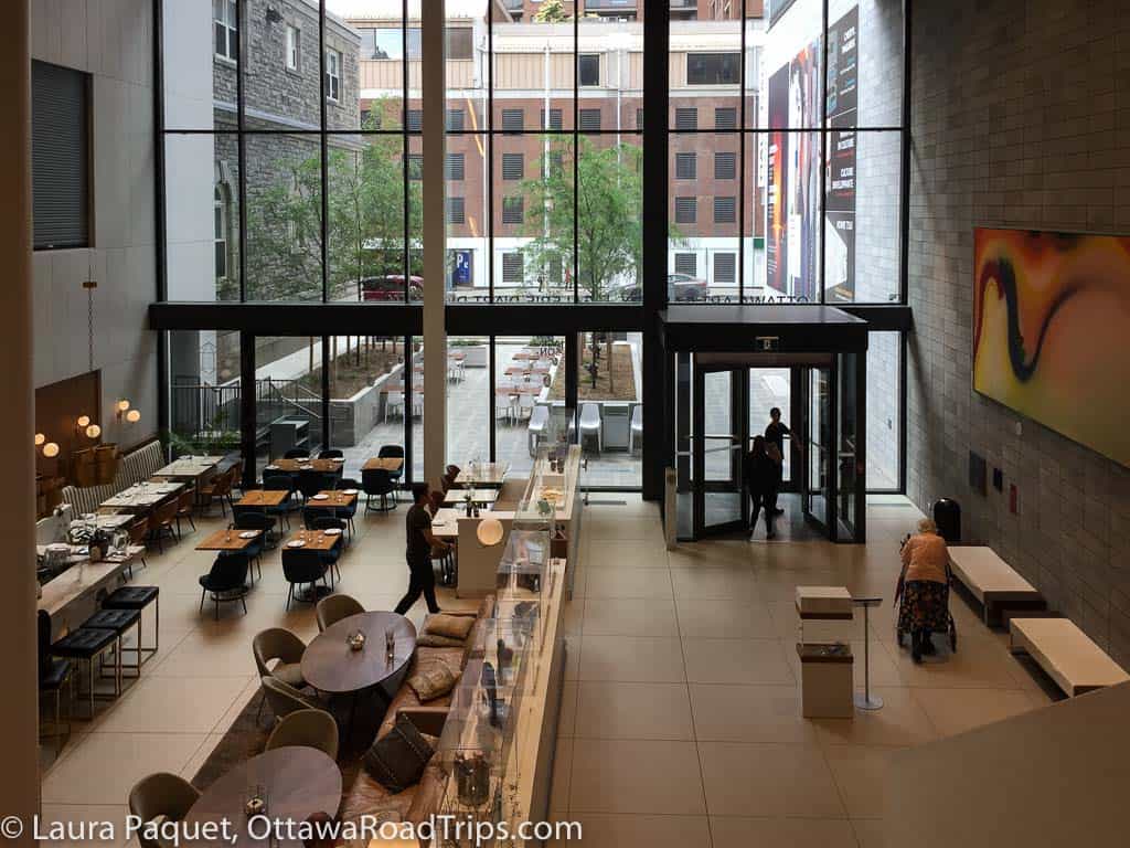 stylish cafe with wooden tables in tall atrium with large wall of windows in the background