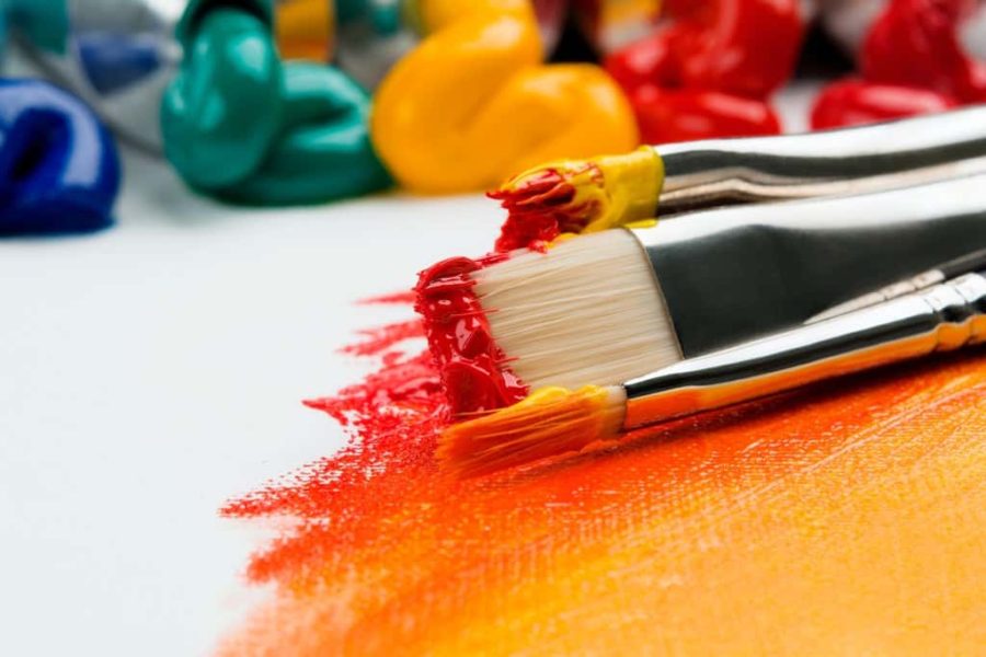 paintbrushes dipped in red paint on top of streaks of yellow, orange and red on a white canvas