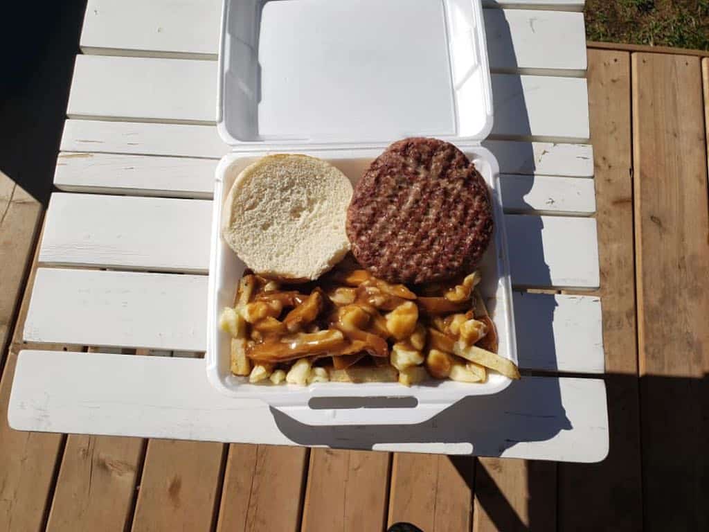 Hamburger and fries in a styrofoam container on a white picnic table.