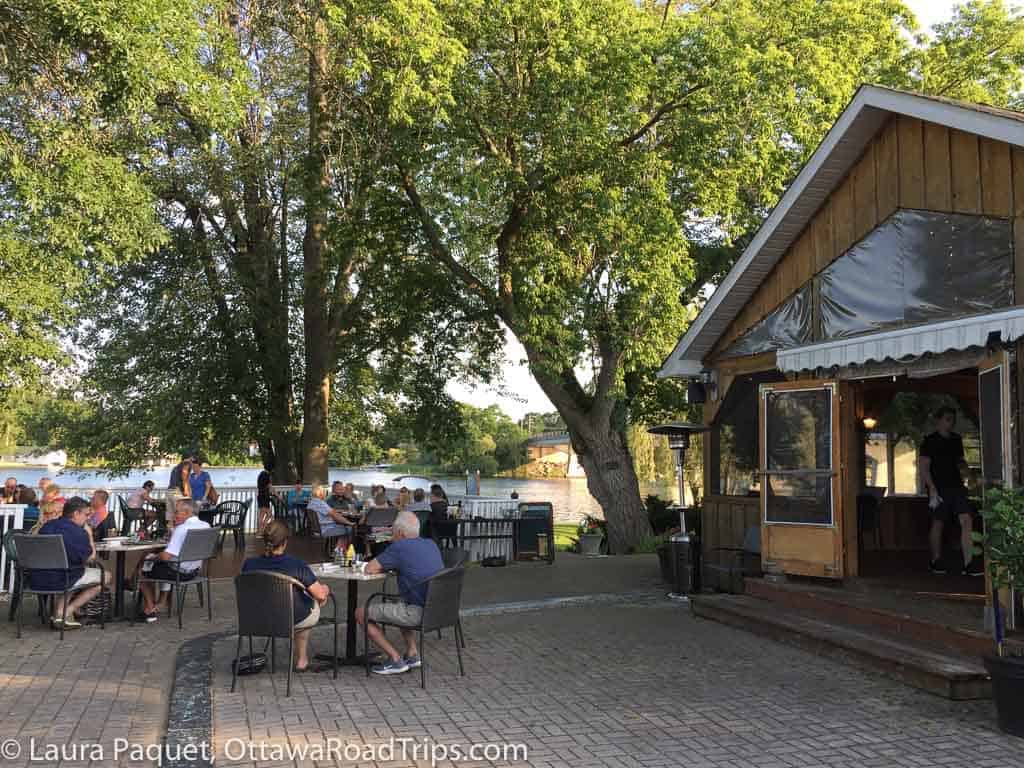 diners on restaurant patio shaded by trees beside a river at cc's on the rideau