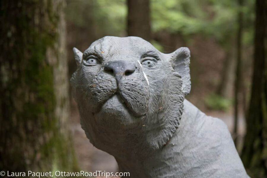 grey stone sculpture of a lion with a forest backdrop