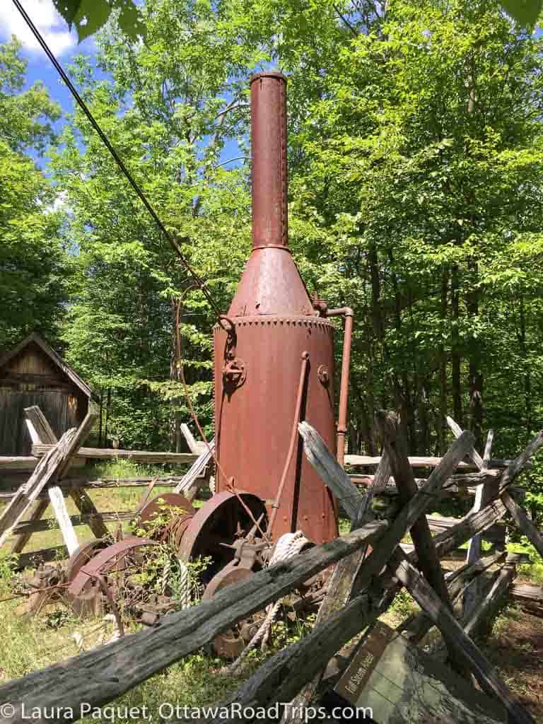 rusted steam equipment behind a split-rail fence