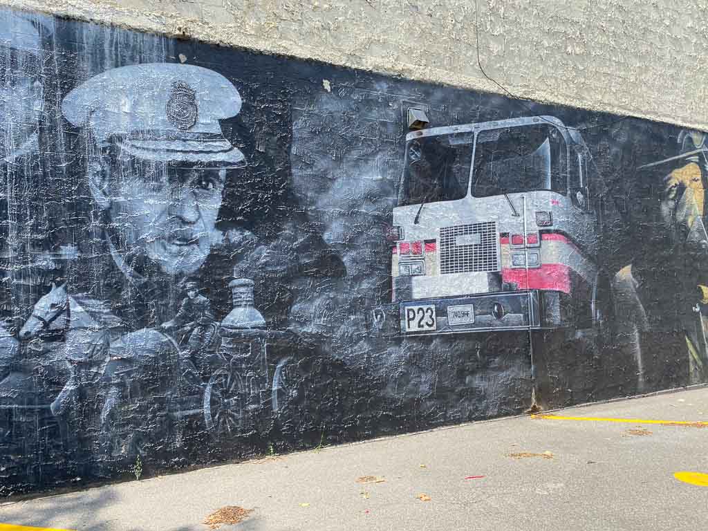 red, white and black mural showing a man in vintage firefighting uniform with old fire truck.