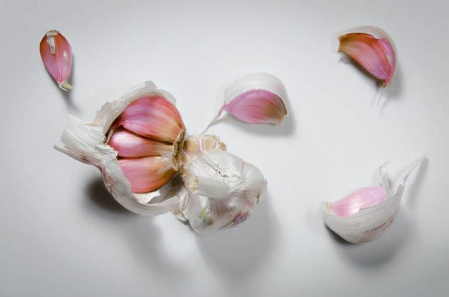 a bulb of garlic split into several pinkish cloves, on a white tabletop