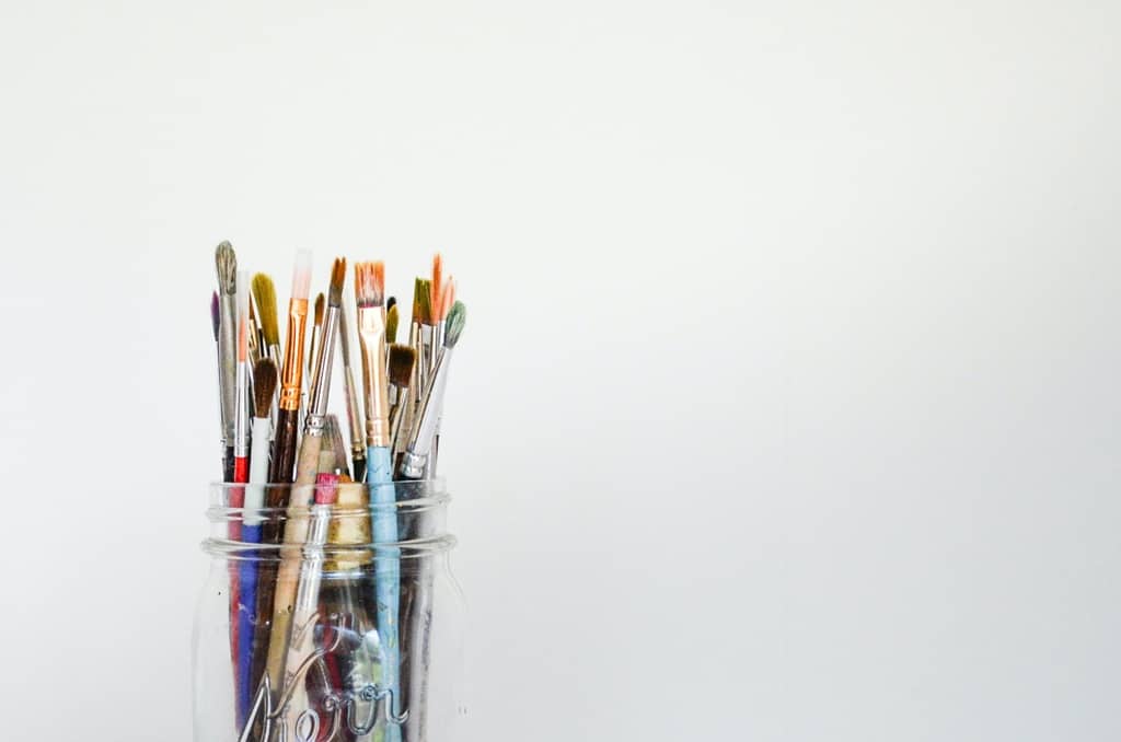 A mason jar full fo paint brushes against a white background.