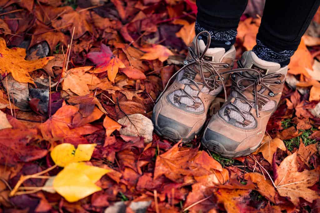 Feet in brown hiking boots amid colourful fallen autumn leaves.