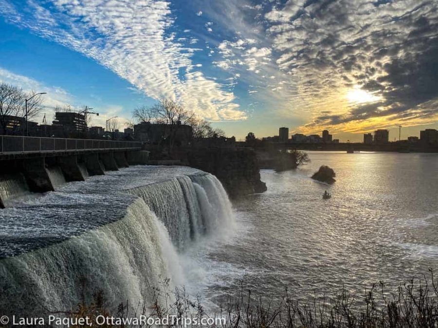 large waterfall at left edge of photo with river at right edge and sunset in background