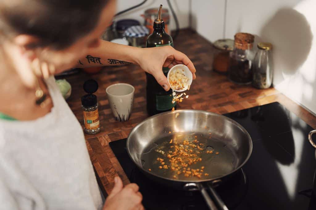 Woman pouring garlic into a silver frying pan of oil.