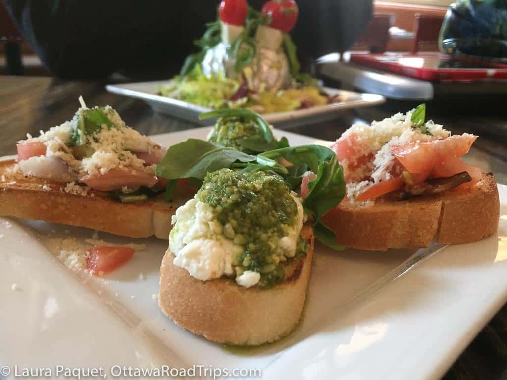 close-up of crostini topped with cheese, pesto, tomatoes and spinach.