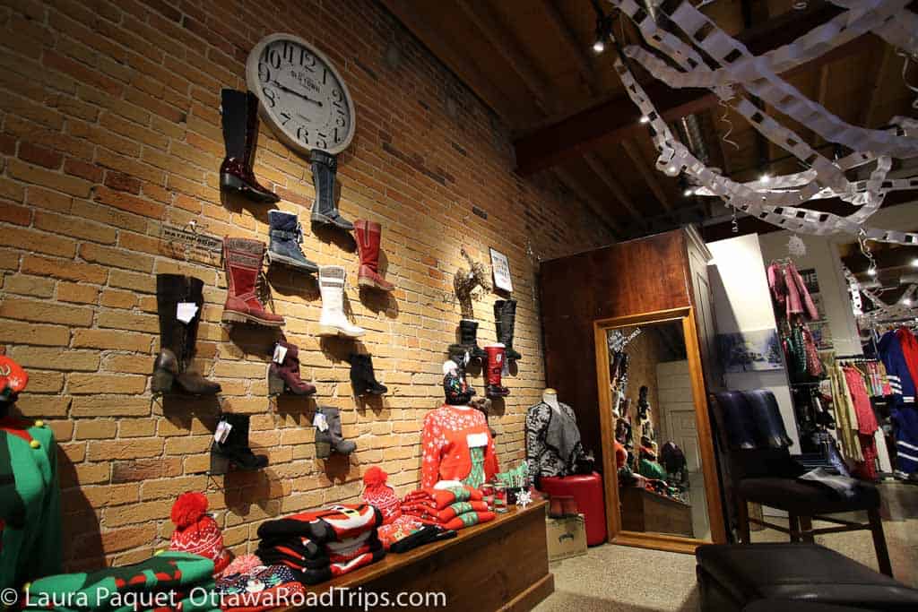 shoes, boots and christmas sweaters displayed against a red brick wall with a large black-and-white clock.