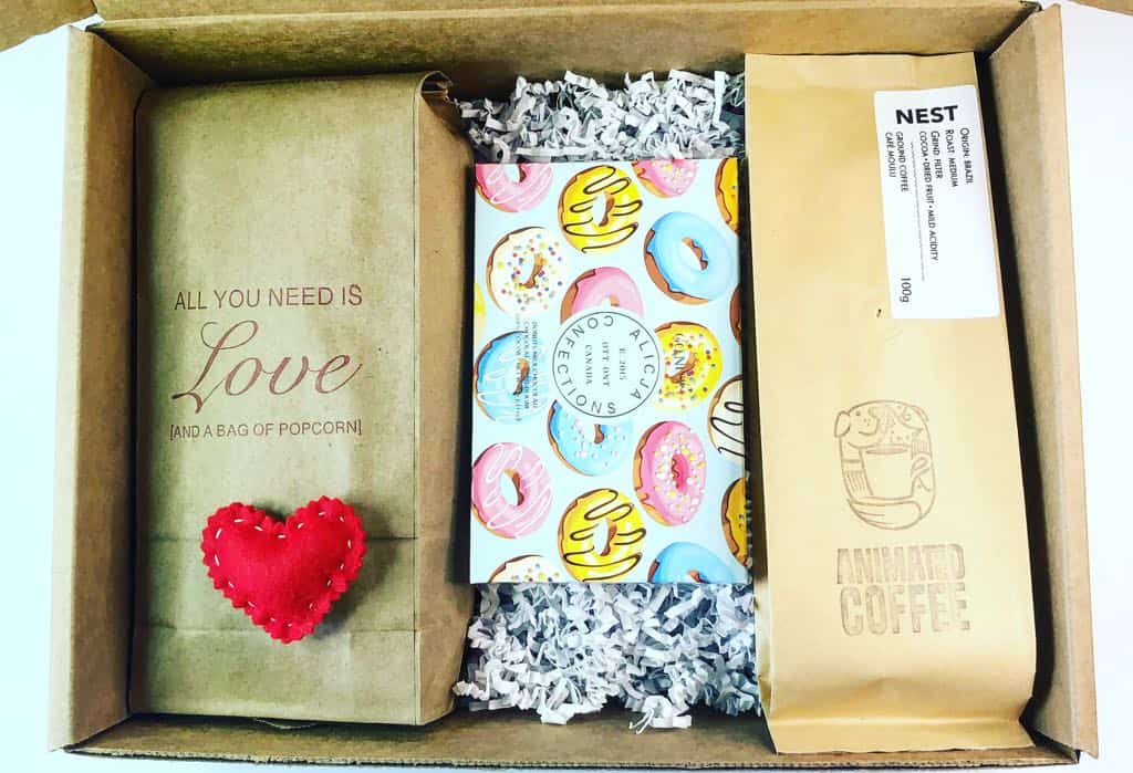 Small cardboard box packed with a bag of popcorn, a small red felt heart, a chocolate bar and a bag of coffee