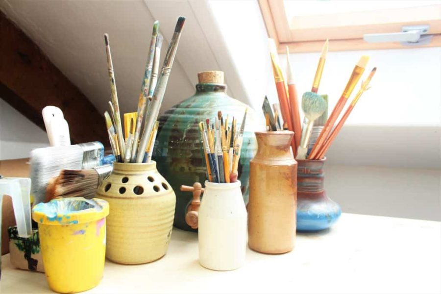 Paintbrushes in jars on a white shelf next to a skylight