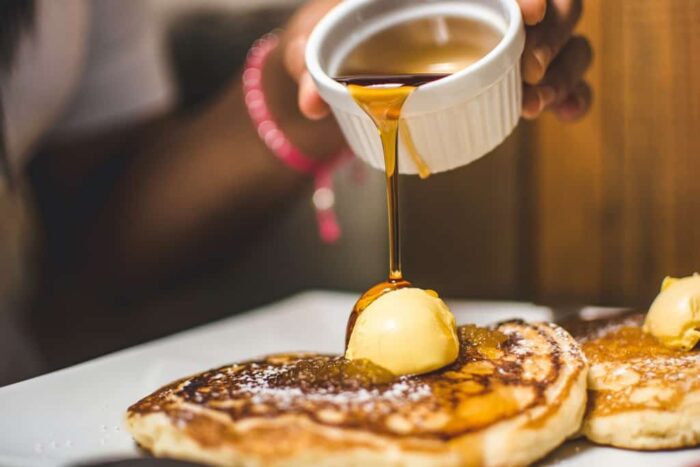 kobby-mendez-pancakes-syrup2-unsplash - Ottawa Road Trips hand pouring maple syrup from a small dish onto a plate of pancakes