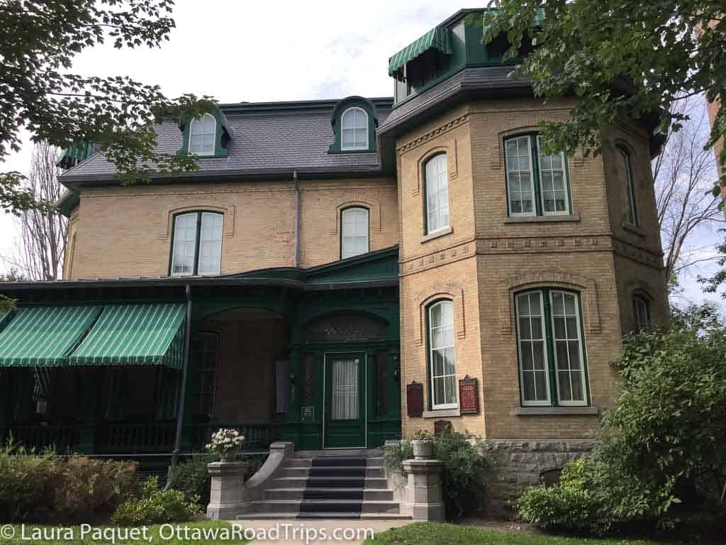 Yellow stone mansion with green awnings, a three-storey tower and mansard roofs