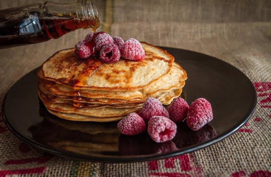 pancakes on a black plate with maple syrup and raspberries